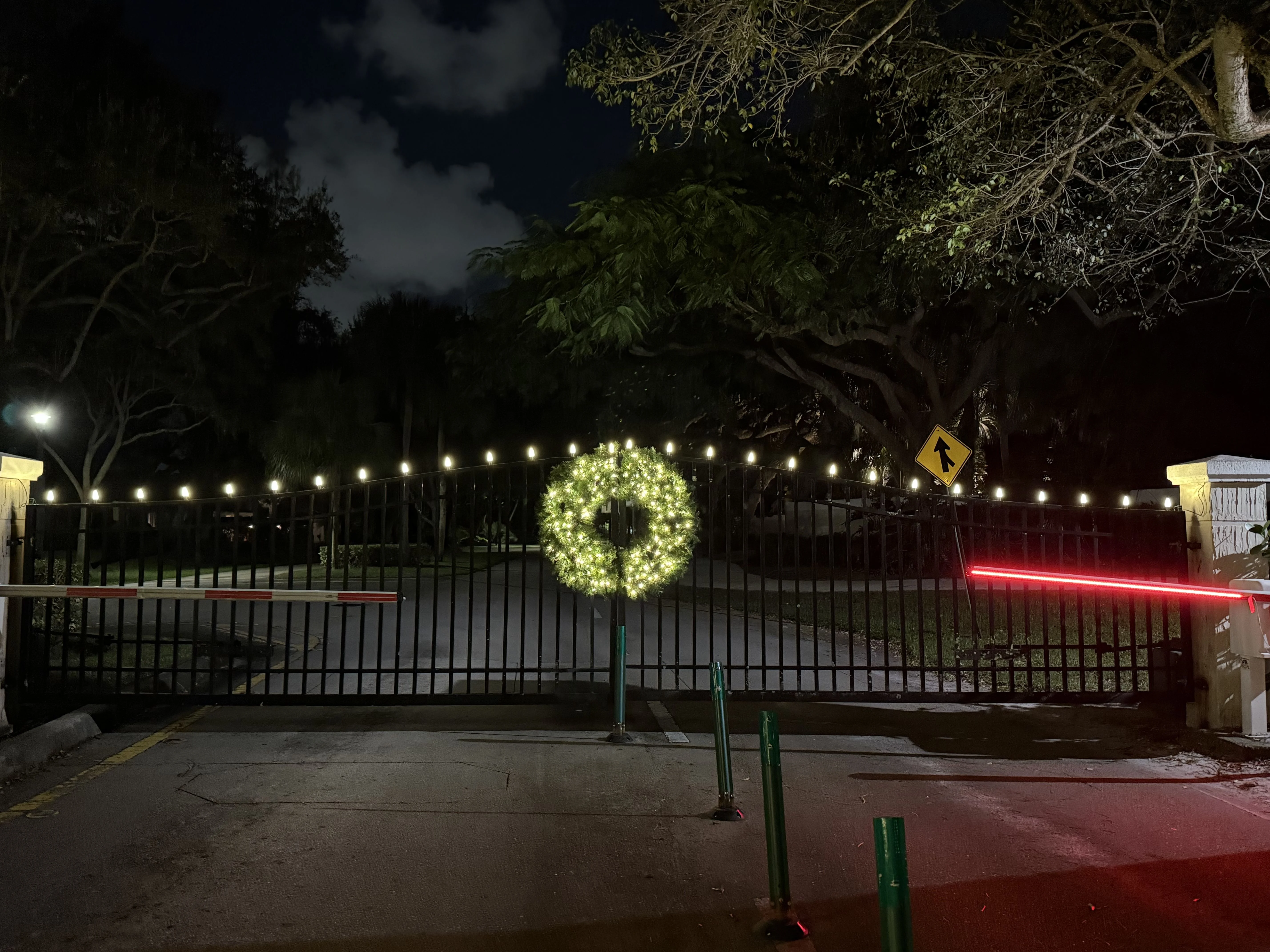 Security gate entrance with large illuminated wreath and string lights for holiday decoration