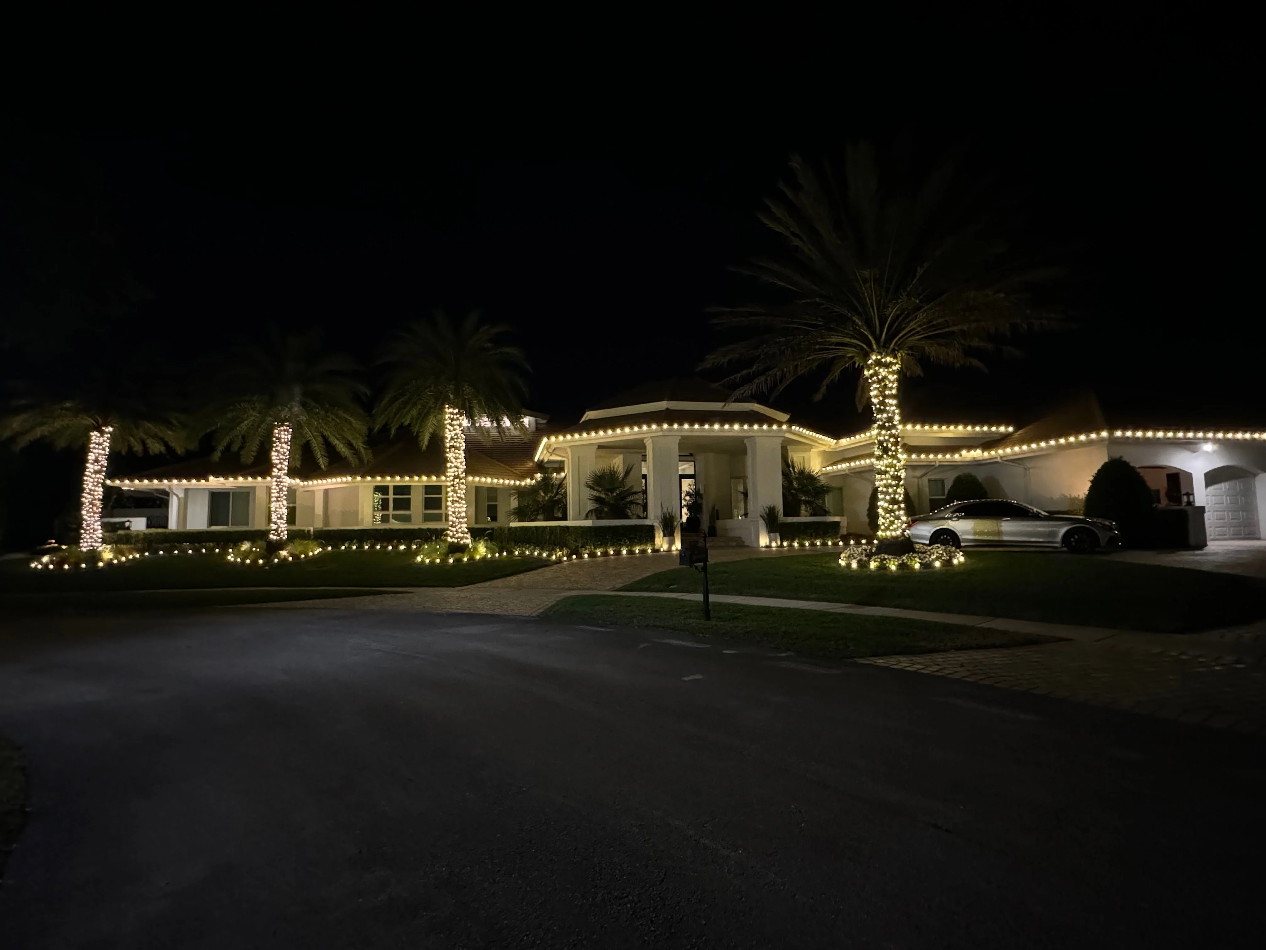 Luxurious modern house with extensive warm white lighting on roofline and palm trees