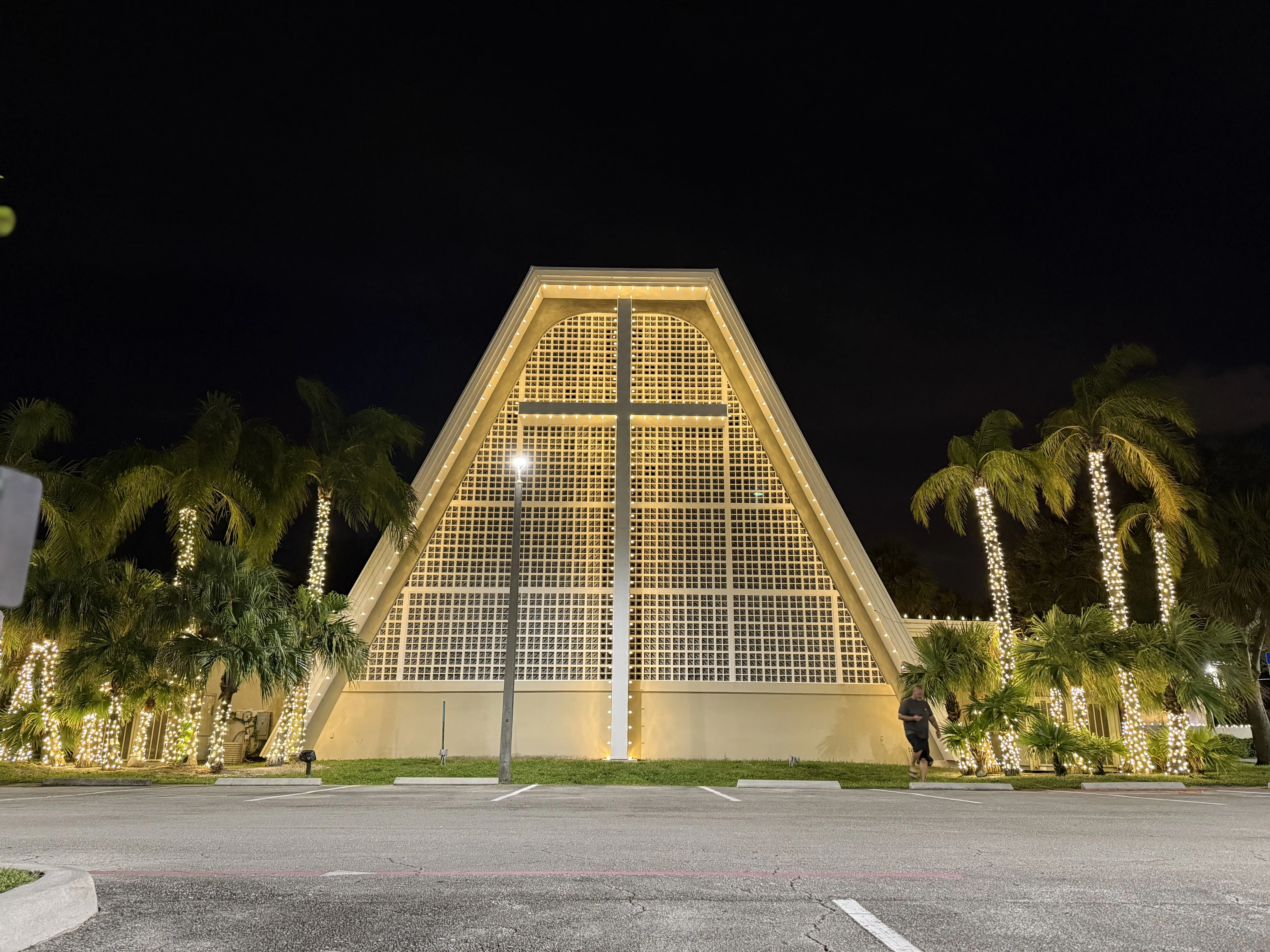 Unique triangular A-frame building with palm trees wrapped in warm white LED lights